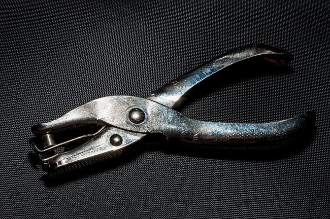 Members Card Hole Punch Hand-held metal Hole Punch laying on dark fabric.