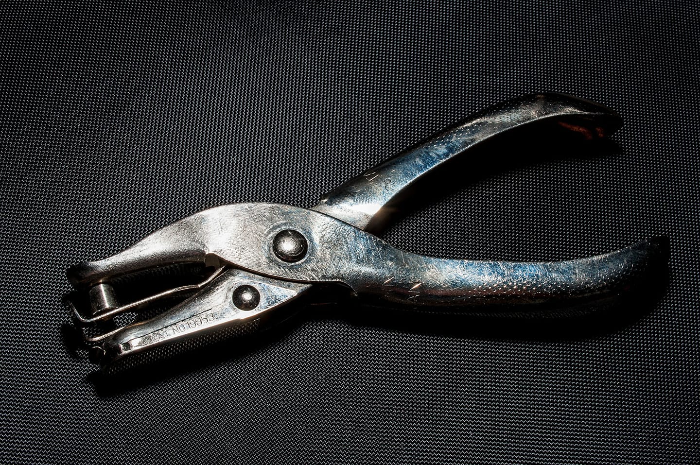 Members Card Hole Punch Hand-held metal Hole Punch laying on dark fabric.