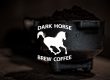 Espresso Portafilter with heaping coffee grounds in the background of a white Dark Horse Brew Logo.