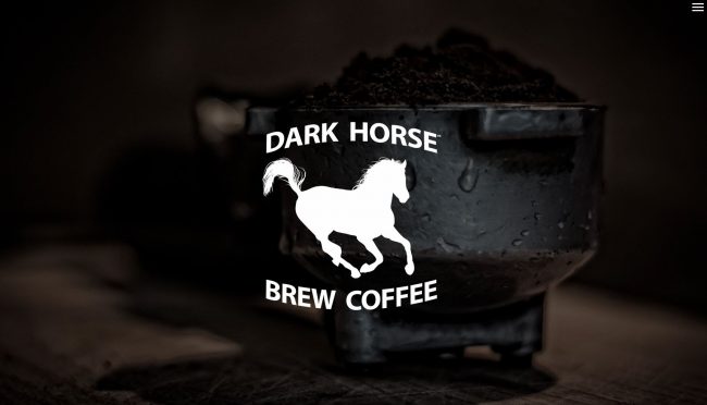 Espresso Portafilter with heaping coffee grounds in the background of a white Dark Horse Brew Logo.
