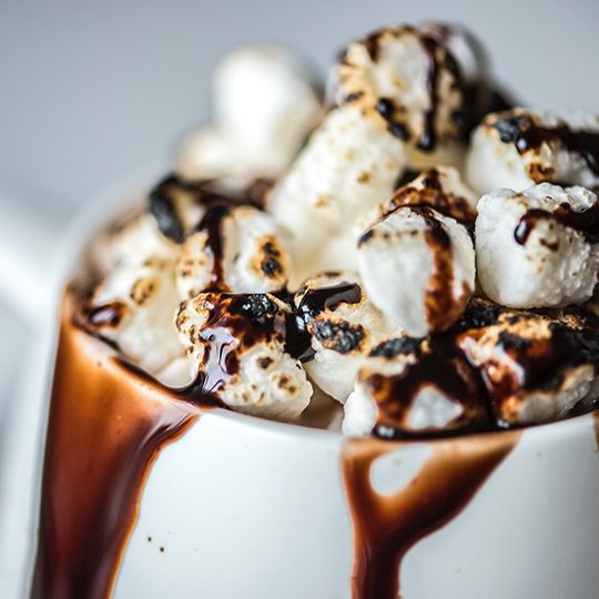 A mug of hot chocolate overflowing with chocolate sauce and mini-sized marshmallows.