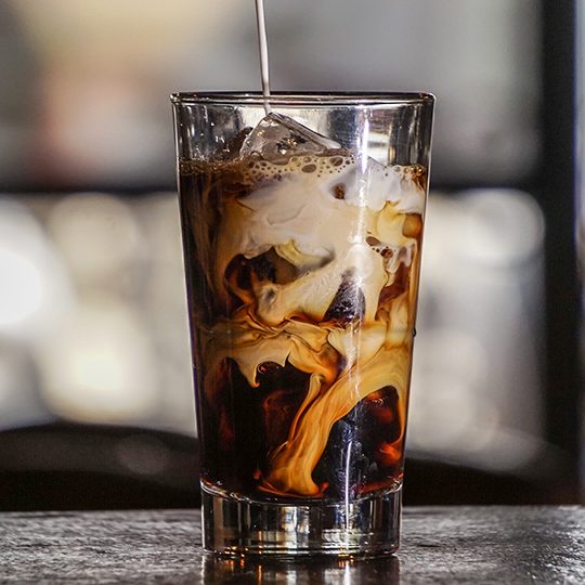 Swirling cream being poured into iced glass of coffee.