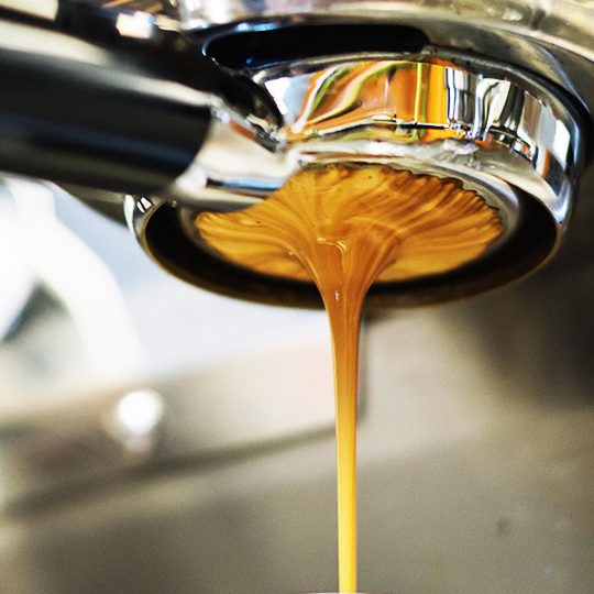 Image of creamy espresso dispensing from portafilter on espresso machine.