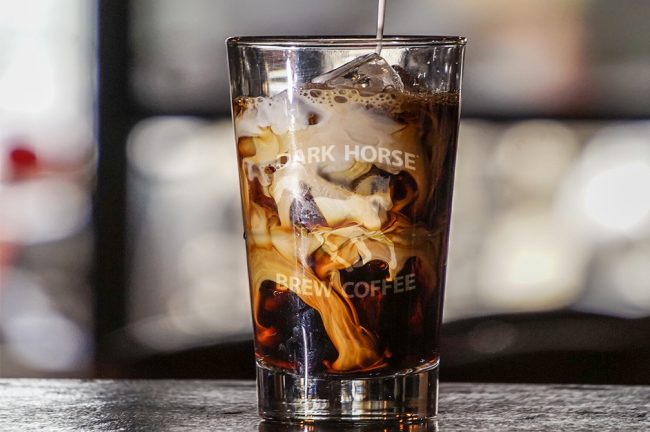 Swirling cream being poured into iced DHBC branded glass of coffee.